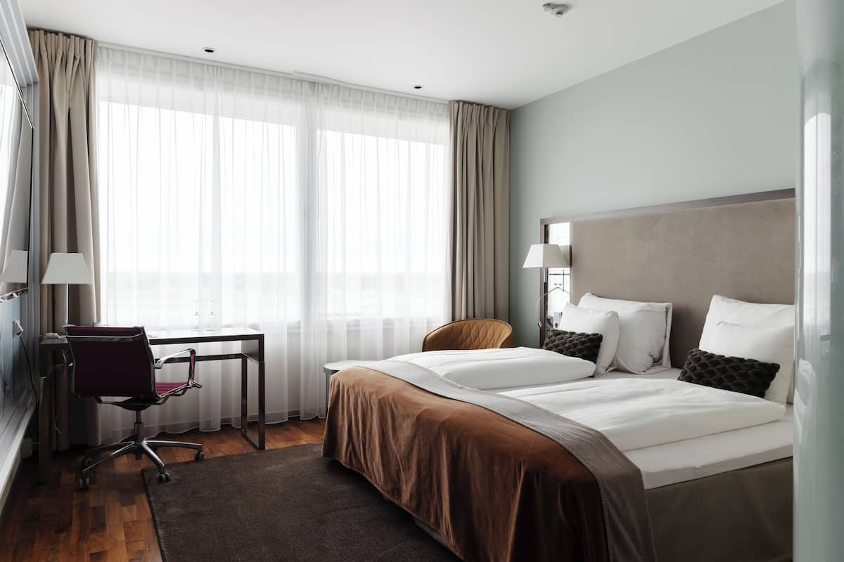 A hotel room with a bed, a desk, a chair, and a window with curtains.
