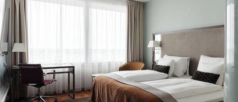 A hotel room with a bed, a desk, a chair, and a window with curtains.