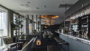 Un área de bar moderna con taburetes altos, una barra y un espacio de estar con sofá y sillones.