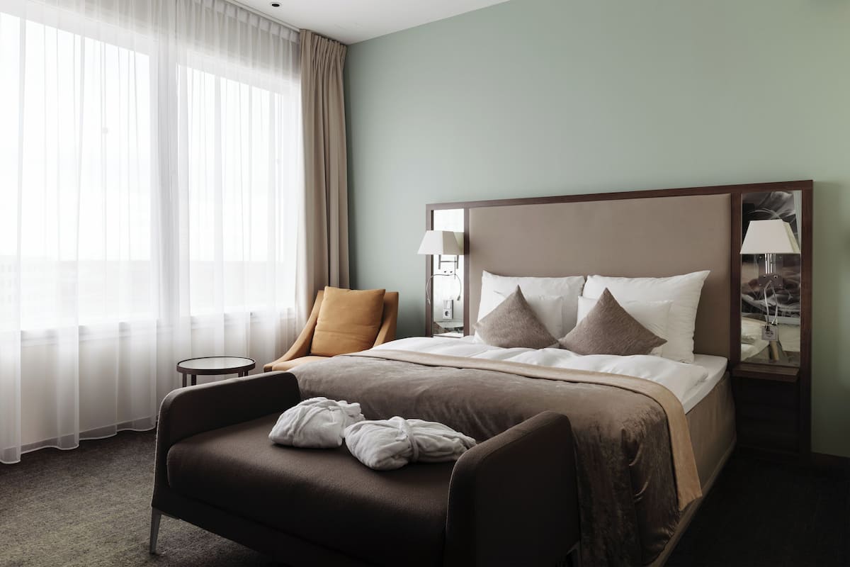 A hotel room with a bed, a chair, a small table, and a mirror.