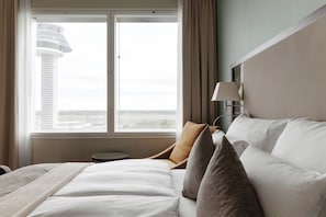 A hotel room with a bed, a nightstand, a lamp, and a window with a view of a cityscape.