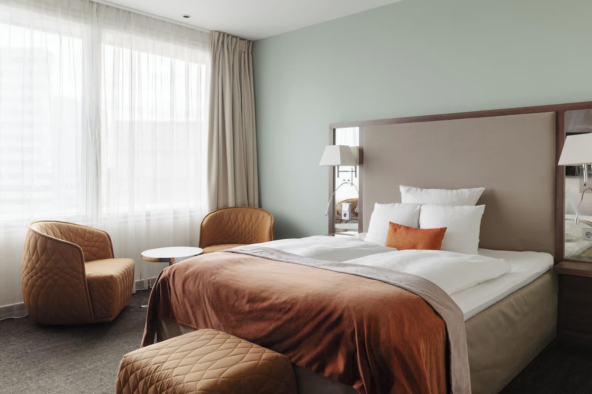 A hotel room with a large bed, a chair, a small table, and a lamp.