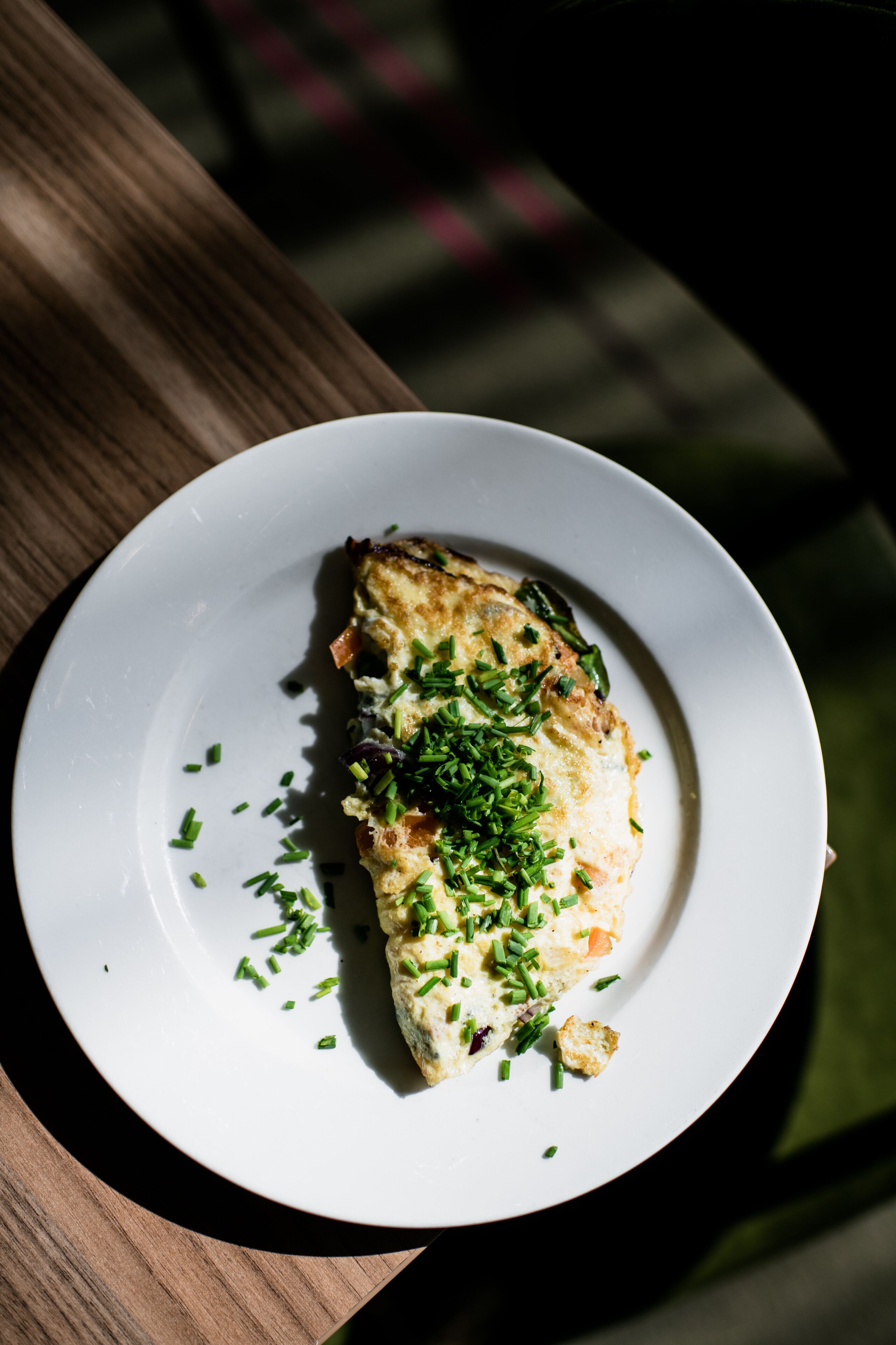 A white plate with a piece of food garnished with green herbs, placed on a wooden table.