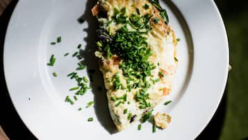 A white plate with a piece of food garnished with green herbs, placed on a wooden table.