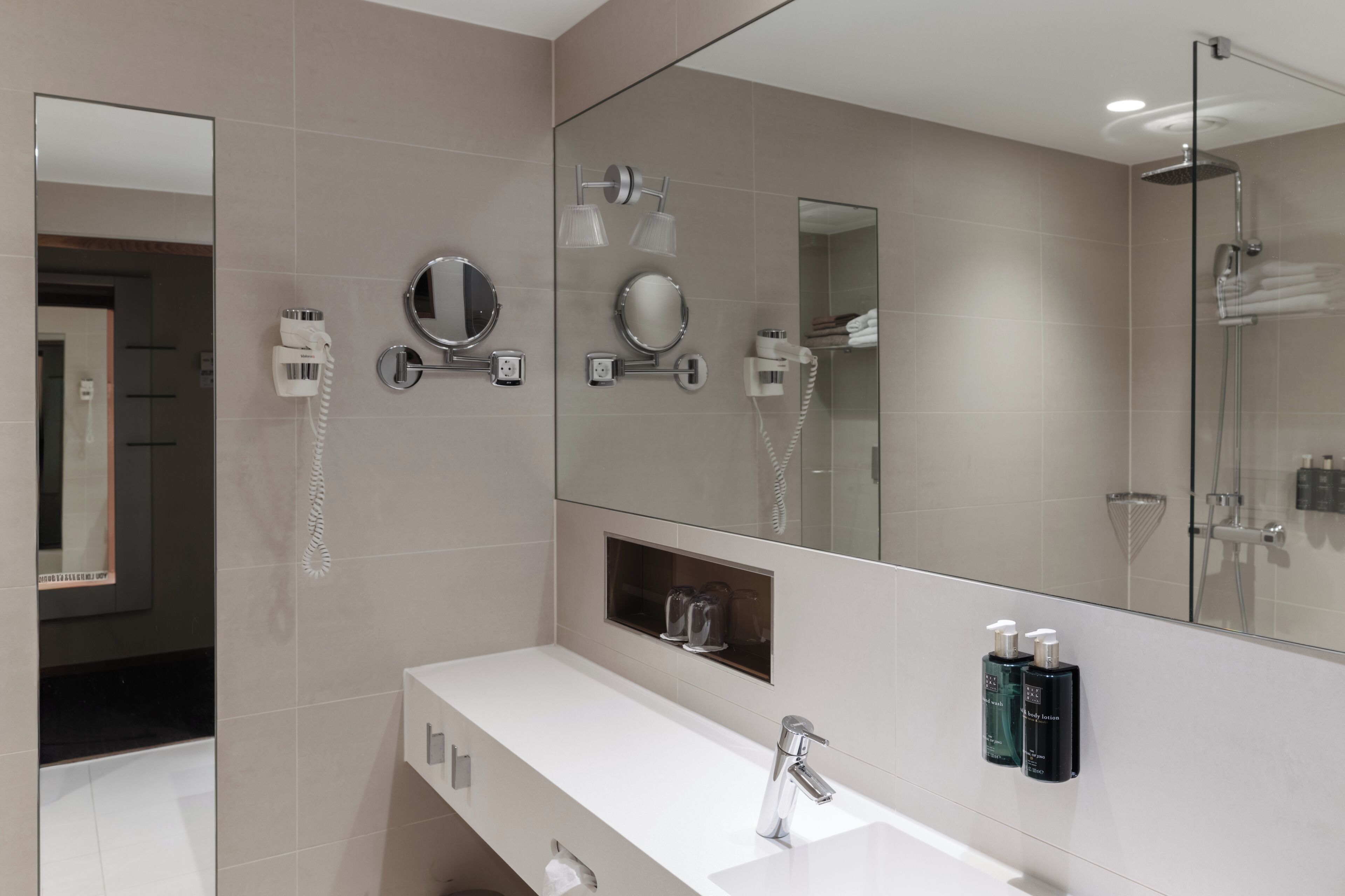 A modern bathroom with a large mirror, a white sink, and a shower area.