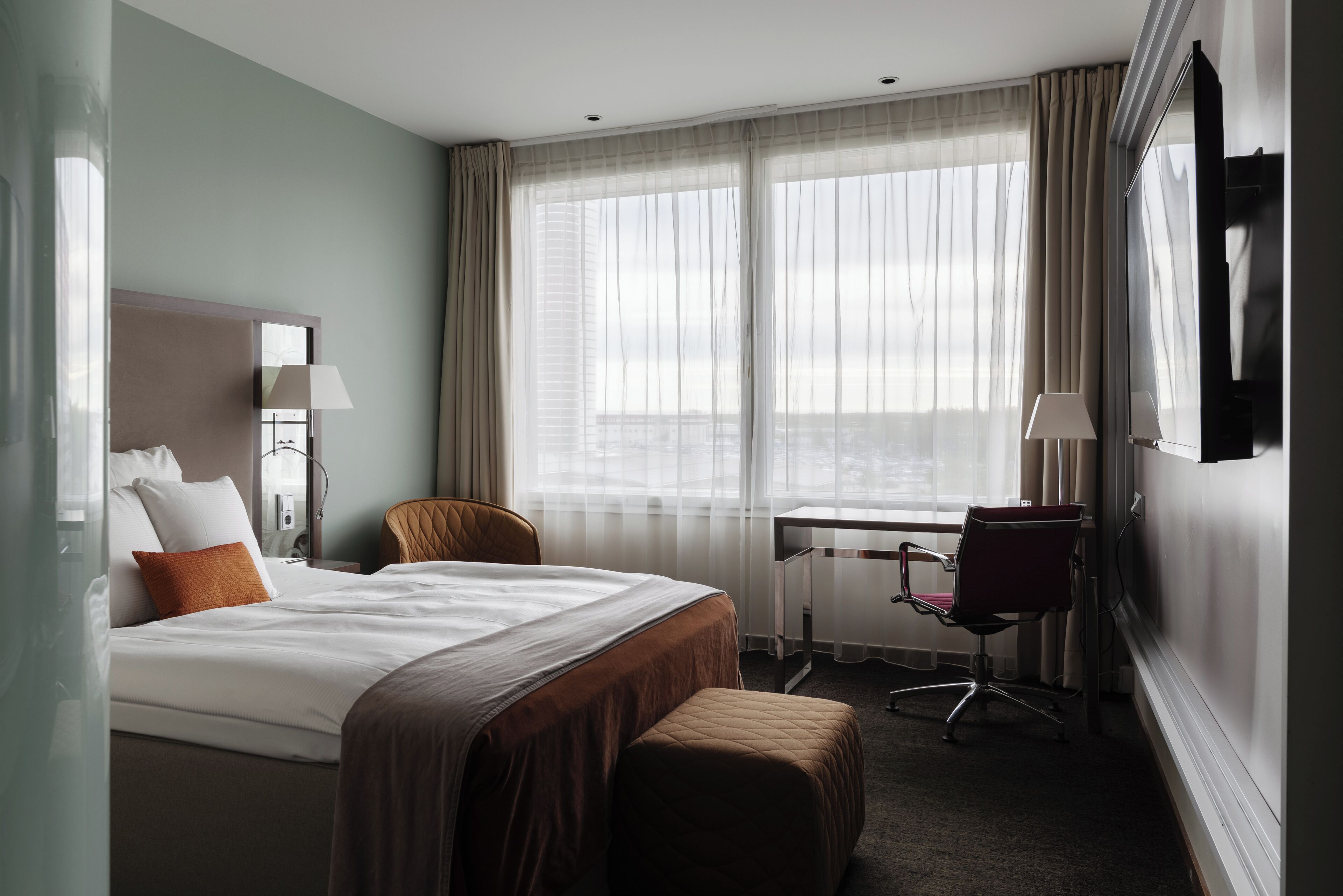 A hotel room with a large bed, a desk, a chair, and a TV.