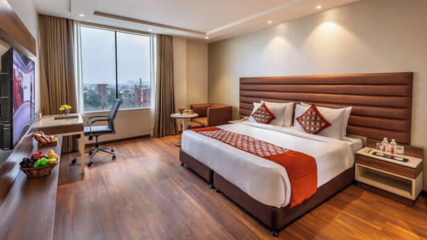 Habitación de hotel con una cama grande, un escritorio, una silla, un televisor y vistas a la ciudad.