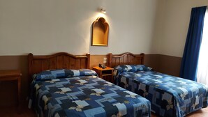 A hotel room with two beds, a bedside table with a phone, a wall-mounted light, and a window with curtains. - Hotel de Talavera (Puebla)
