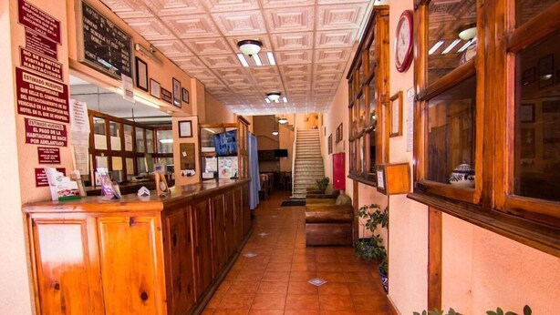 A hotel lobby with a wooden reception desk, a staircase, and a clock on the wall. - Hotel De Talavera (Puebla)