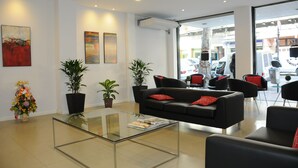 En moderne hotellobby med et glasbord, sorte sofaer med røde puder, plantekasser og kunst på væggene.