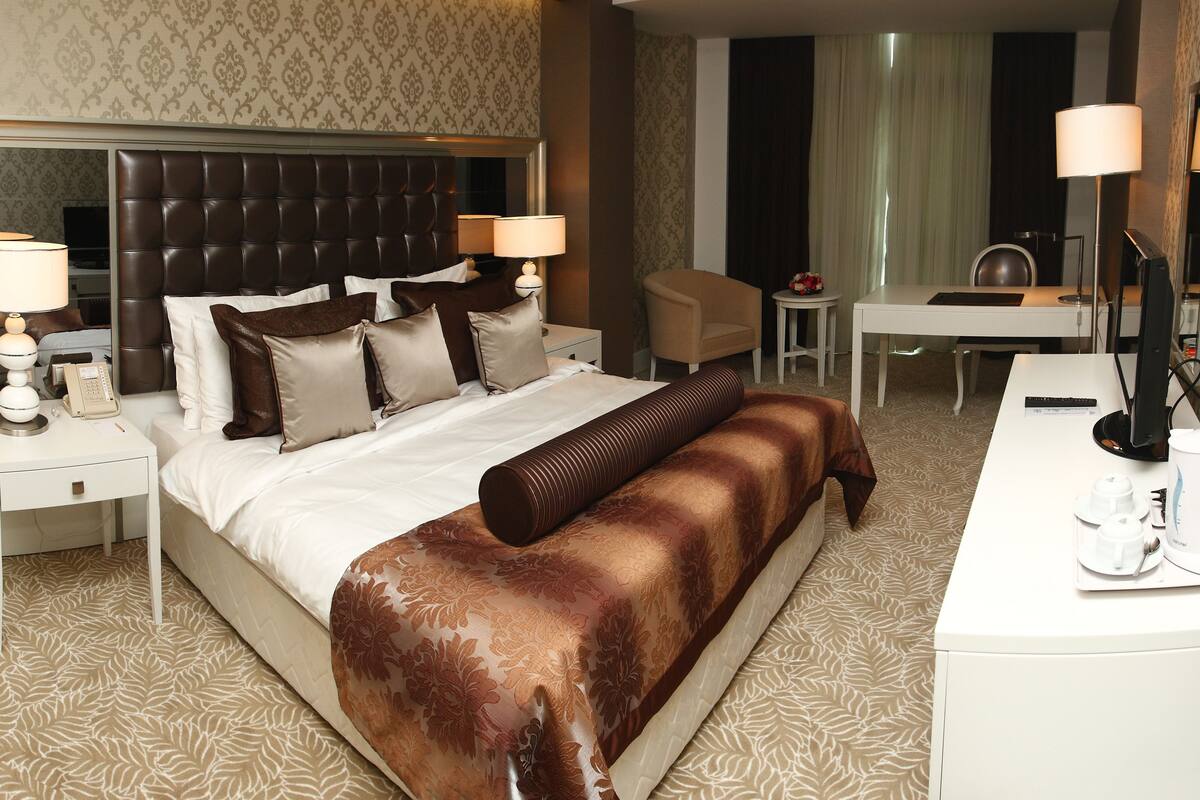 Ein Hotelzimmer mit einem großen Bett, einem Schreibtisch, einem Stuhl, einer Kaffeemaschine und einem Spiegel.