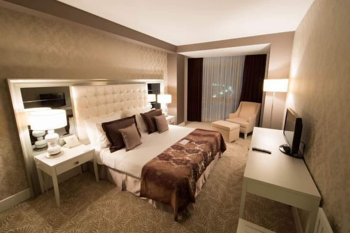 Ein Hotelzimmer mit einem großen Bett, einem Schreibtisch, einem Stuhl, einem Fernseher und einem Fenster mit Vorhängen.