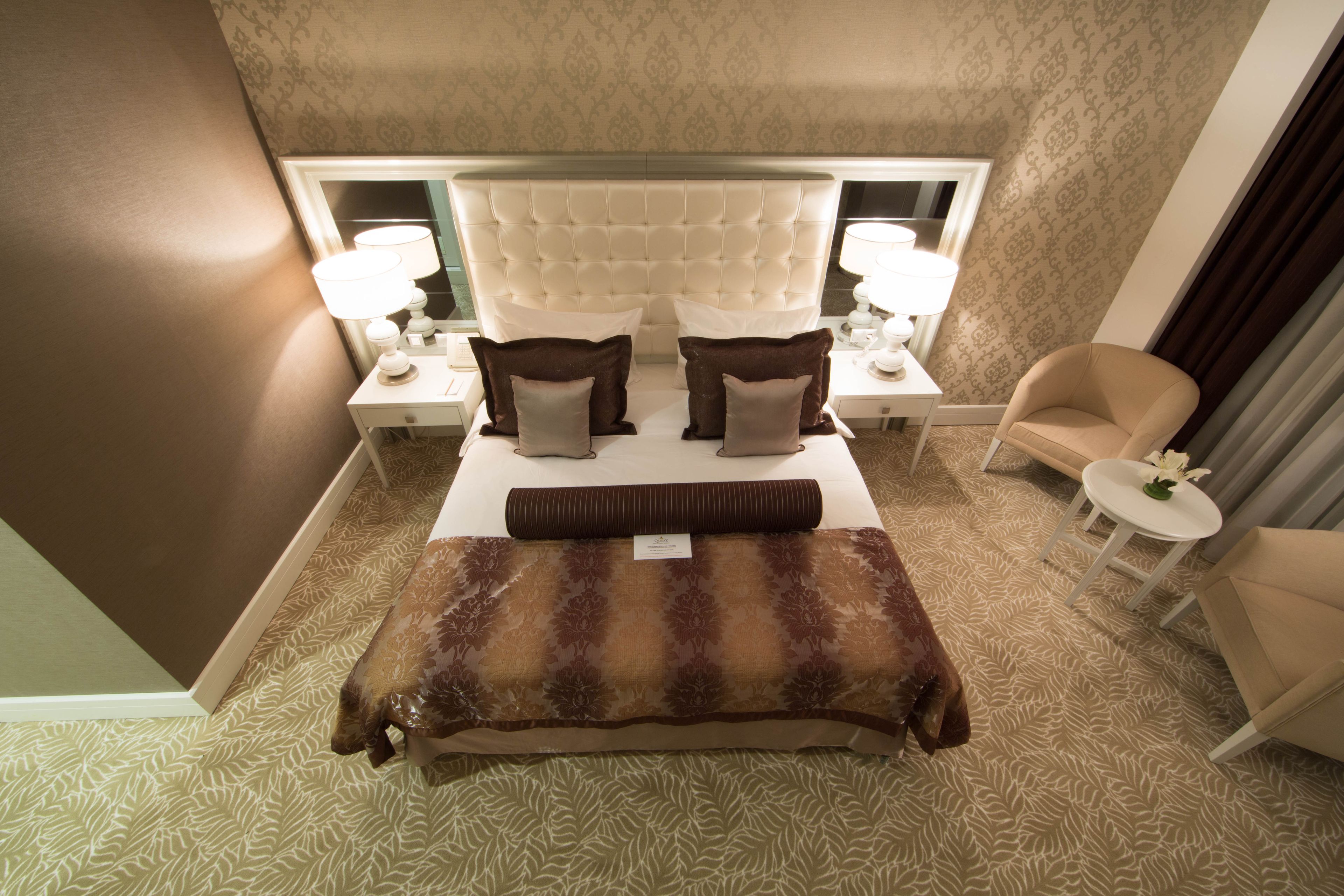 Ein Hotelzimmer mit einem großen Bett, zwei Nachttischlampen, einem kleinen runden Tisch mit einer Blume und einem Sessel.