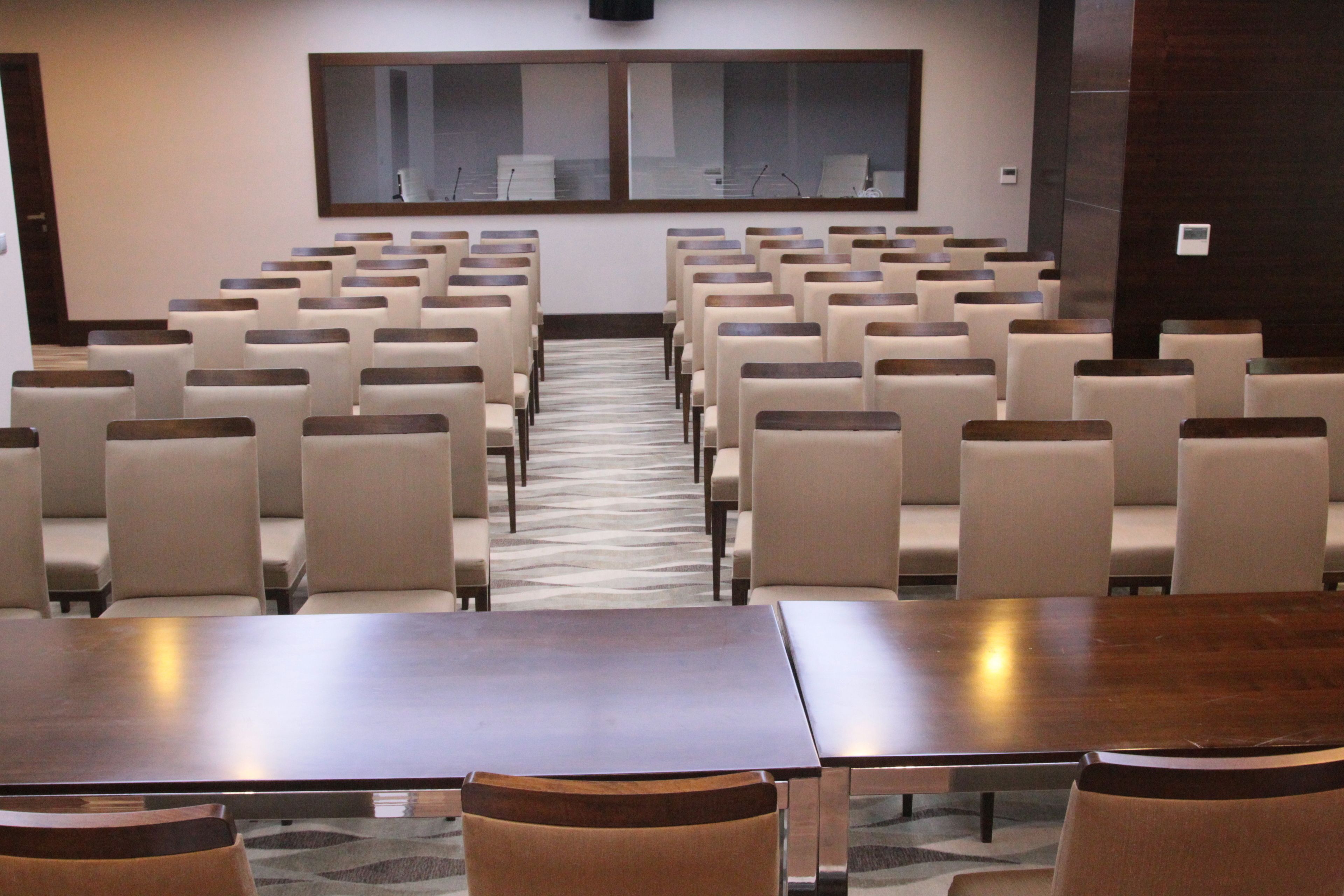 A conference room with rows of chairs and tables, a carpeted floor, and a large window at the front.
