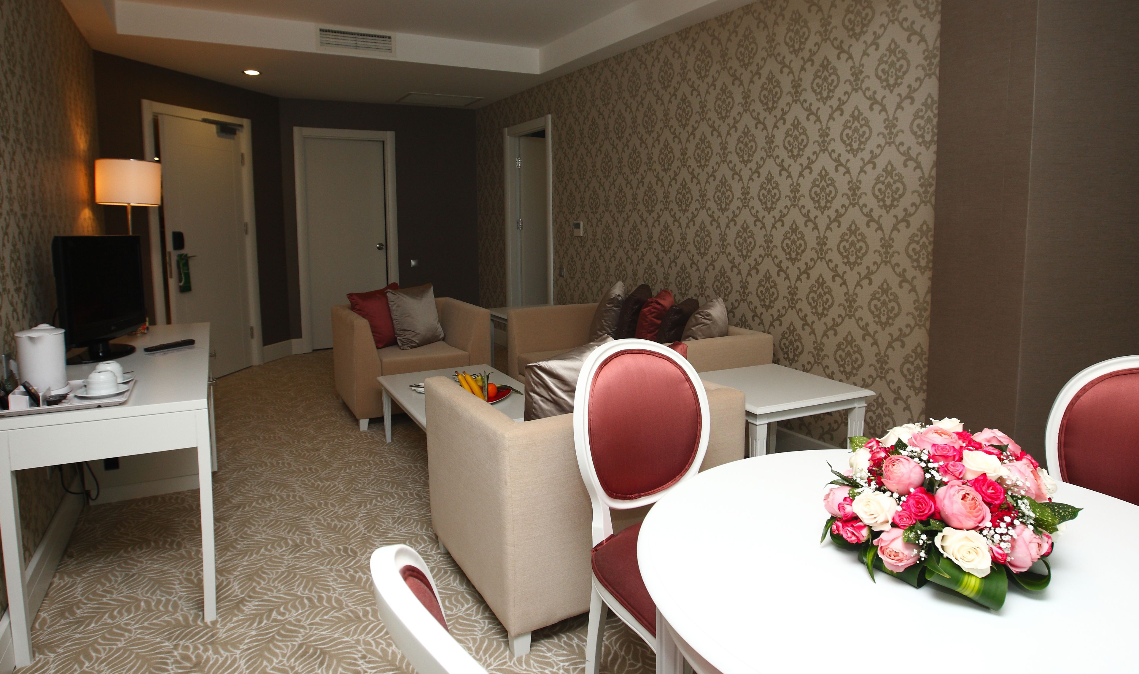 Une chambre d’hôtel avec un canapé, une table à manger avec des chaises, un téléviseur et un arrangement floral.