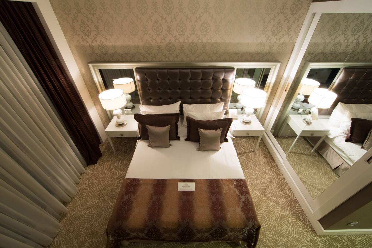 Ein Hotelzimmer mit einem großen Bett, zwei Nachttischen mit Lampen, einem Spiegel und einem gemusterten Teppich.