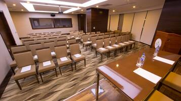 Un salón de conferencias con filas de sillas, una mesa larga y suelo alfombrado.