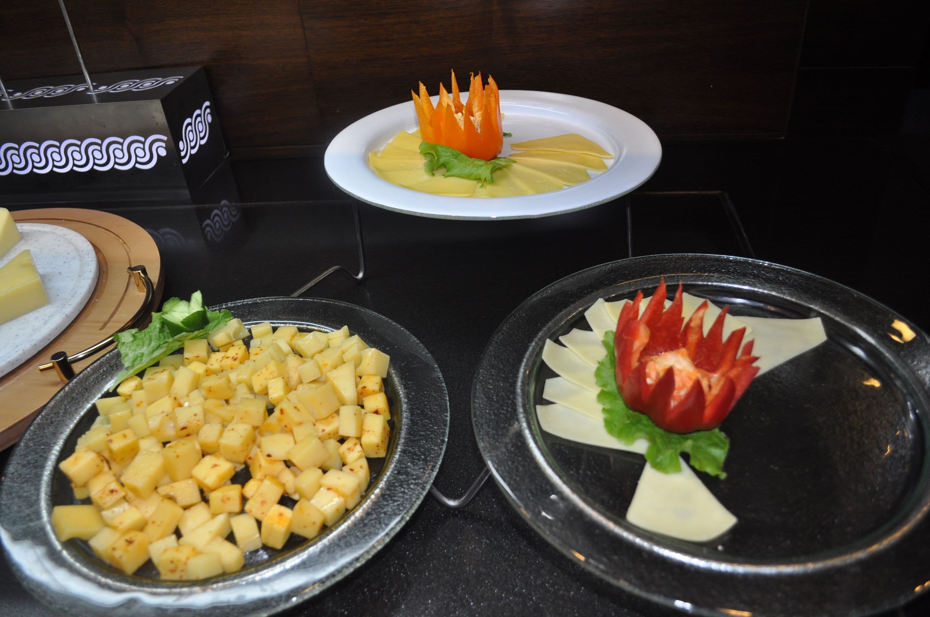 Un buffet proposant une variété de plats, notamment des pommes de terre coupées en dés, un arrangement de fruits décoratif et une assiette ornée d’un motif original.