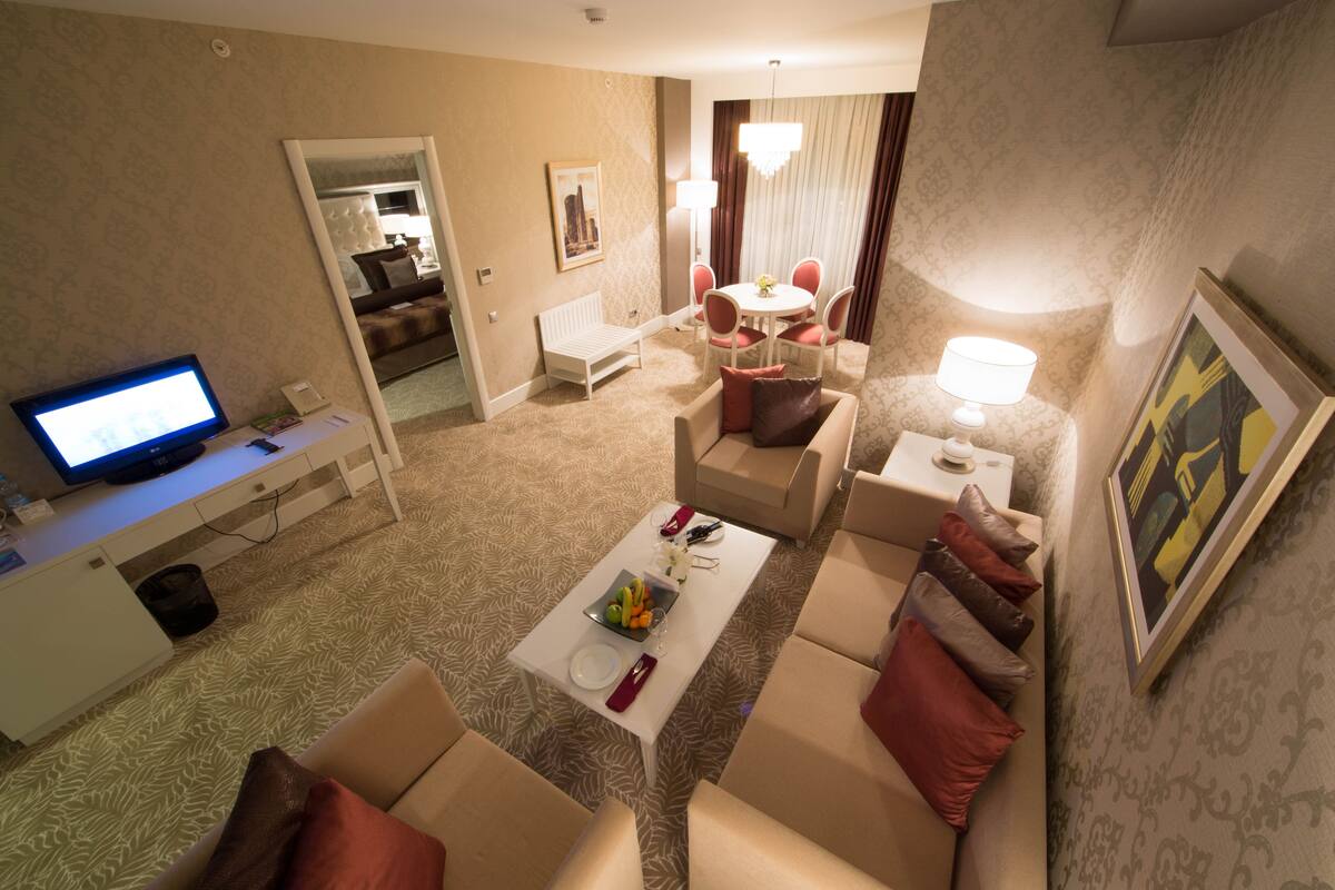 Ein Hotelzimmer mit Fernseher, Essbereich mit Tisch und Stühlen, einer Couch und einer Lampe.