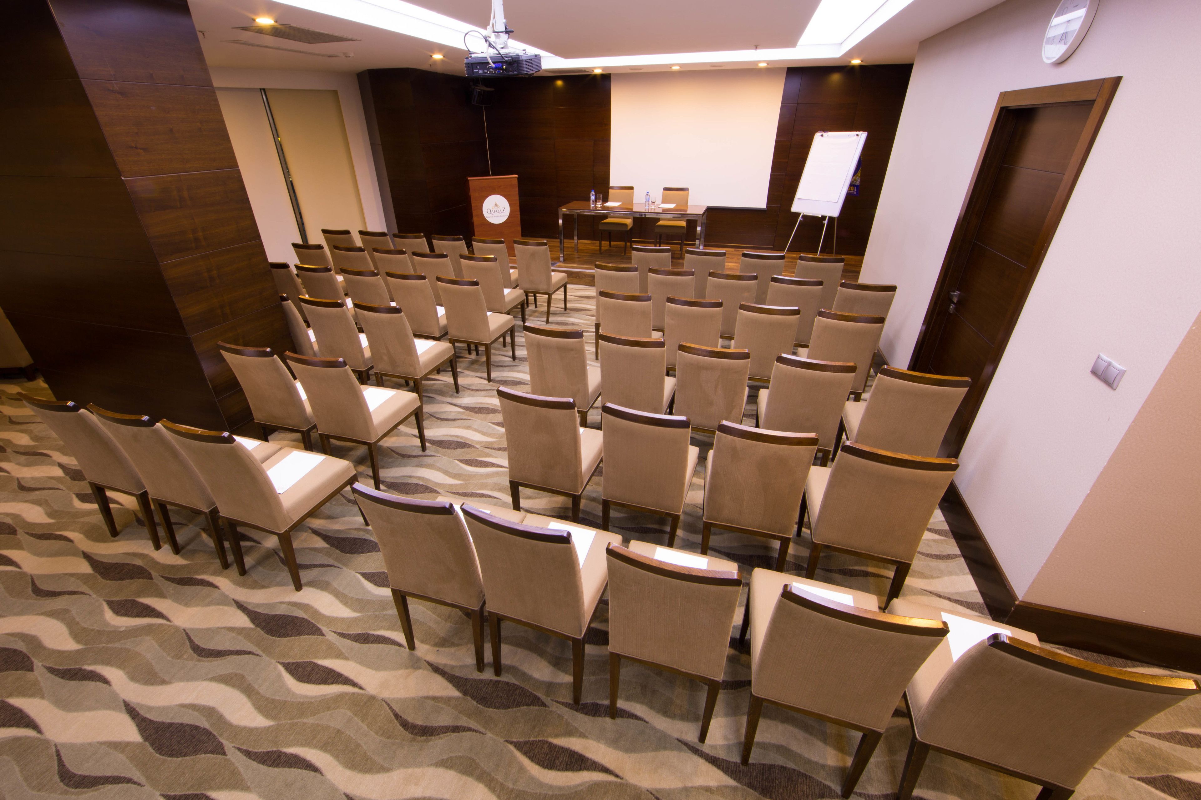 Une salle de conférence avec des rangées de chaises, un pupitre, un écran de projection et un tableau blanc.