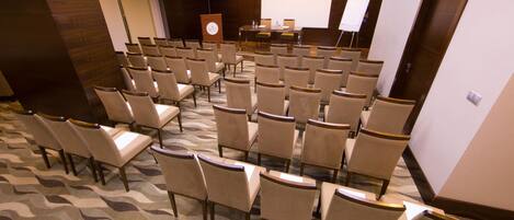 Une salle de conférence avec des rangées de chaises, un pupitre, un écran de projection et un tableau blanc.