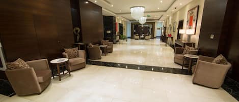 A spacious lobby with a high ceiling, a chandelier, and multiple seating areas with tables and chairs.