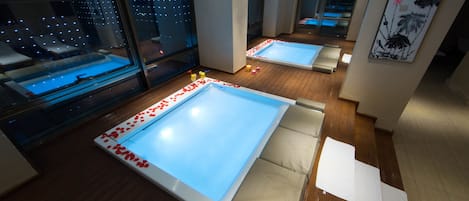 A modern spa room with two large soaking tubs, wooden flooring, and large windows with city views.