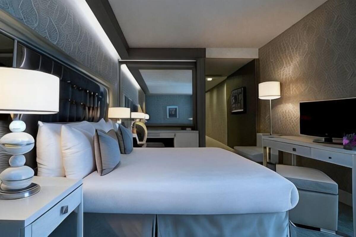 Ein Hotelzimmer mit einem großen Bett, Nachttischlampen, einem Fernseher und einem Schreibtisch mit Lampe.