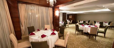 A dining area with round tables, chairs, and a chandelier.