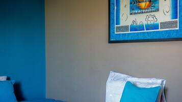 Habitación de hotel con una cama que tiene una colcha y almohadas de diseño azul, una pared con una obra de arte enmarcada, y una pared lisa al fondo.