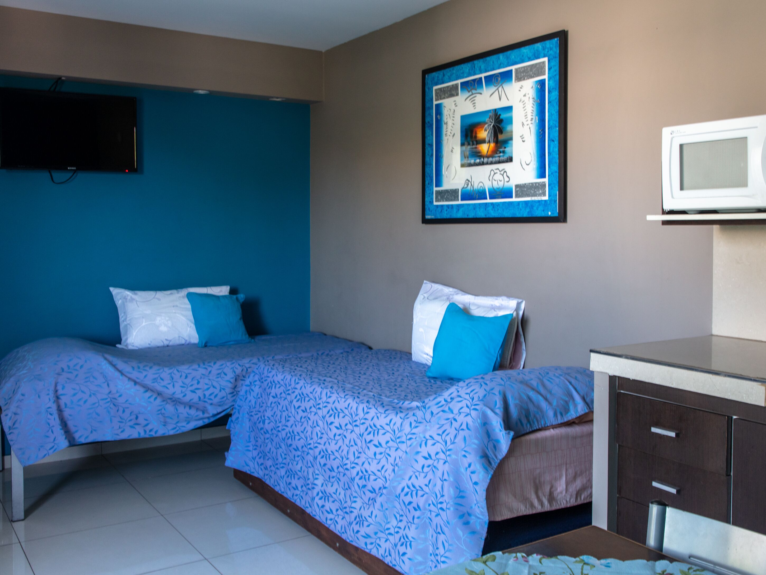 A hotel room with two beds, a TV, a microwave, and a framed artwork on the wall.