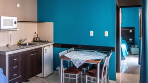 A compact kitchen with a microwave, sink, and stove, a dining table with chairs, and a view into a bedroom with a bed and nightstand. - Paradise Departamentos (Mendoza)