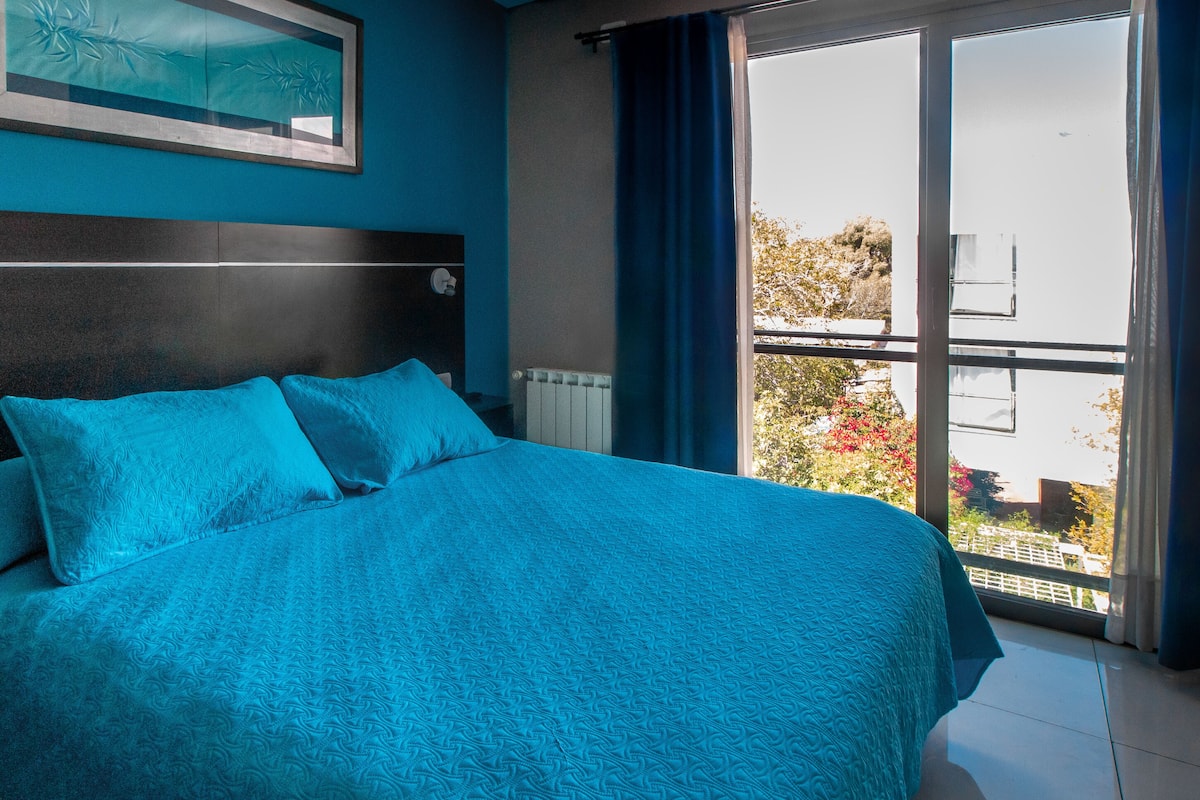 Ein Schlafzimmer mit einem großen Bett, einem Fenster mit Vorhängen und Blick nach draußen.