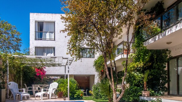 A modern building with a swimming pool, outdoor seating, and lush greenery. - Paradise Departamentos (Mendoza)