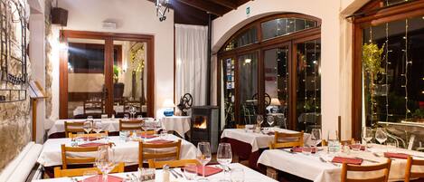 Un restaurant doté de nombreuses tables dressées pour le service, avec un mur en pierre et des poutres en bois.