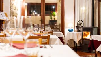 A dining area with tables set for a meal, a wood-burning stove, and a view of the outdoors.