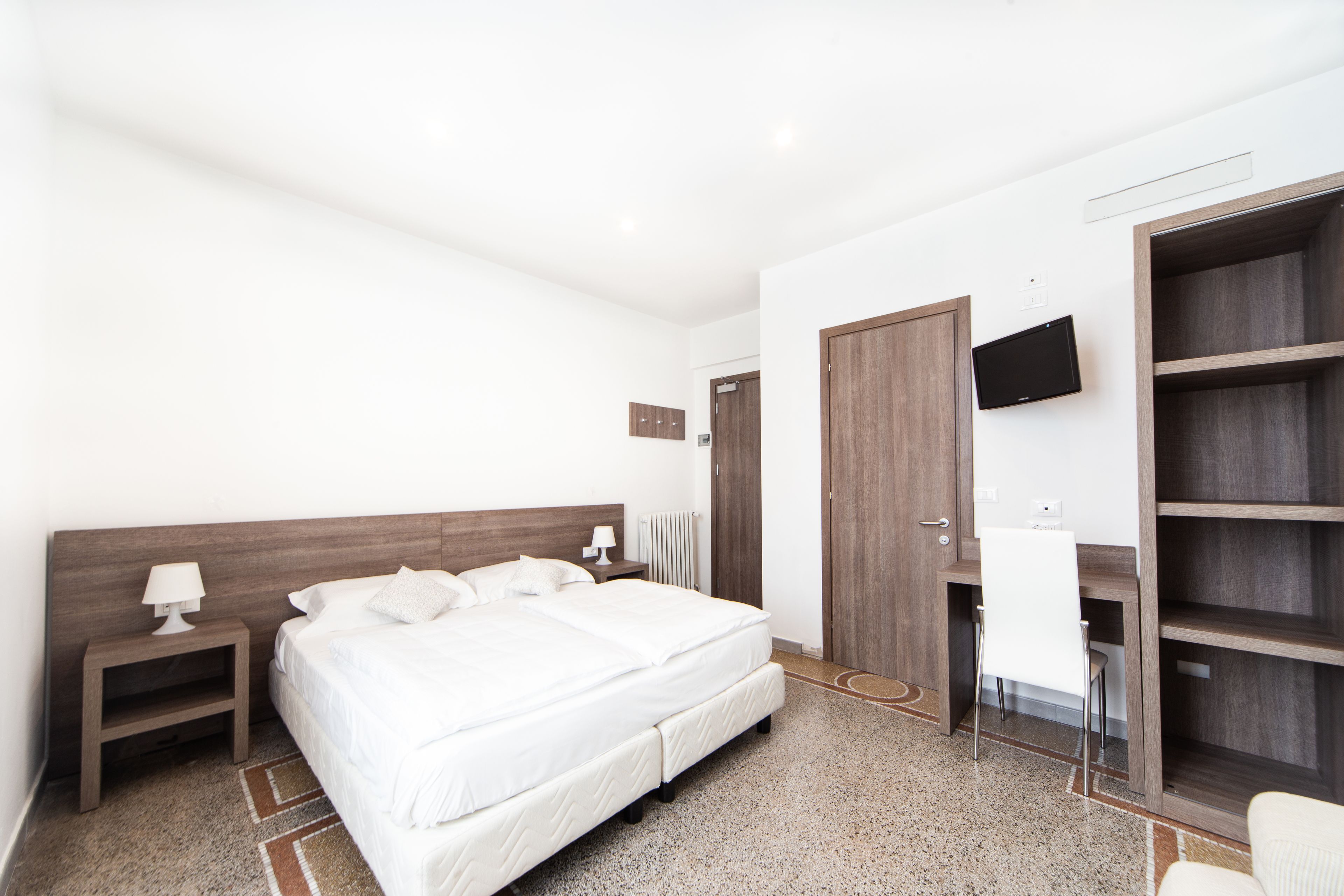 Een moderne hotelkamer met een groot bed, een nachtkastje met een lamp, een aan de muur bevestigde televisie en een kledingkast.