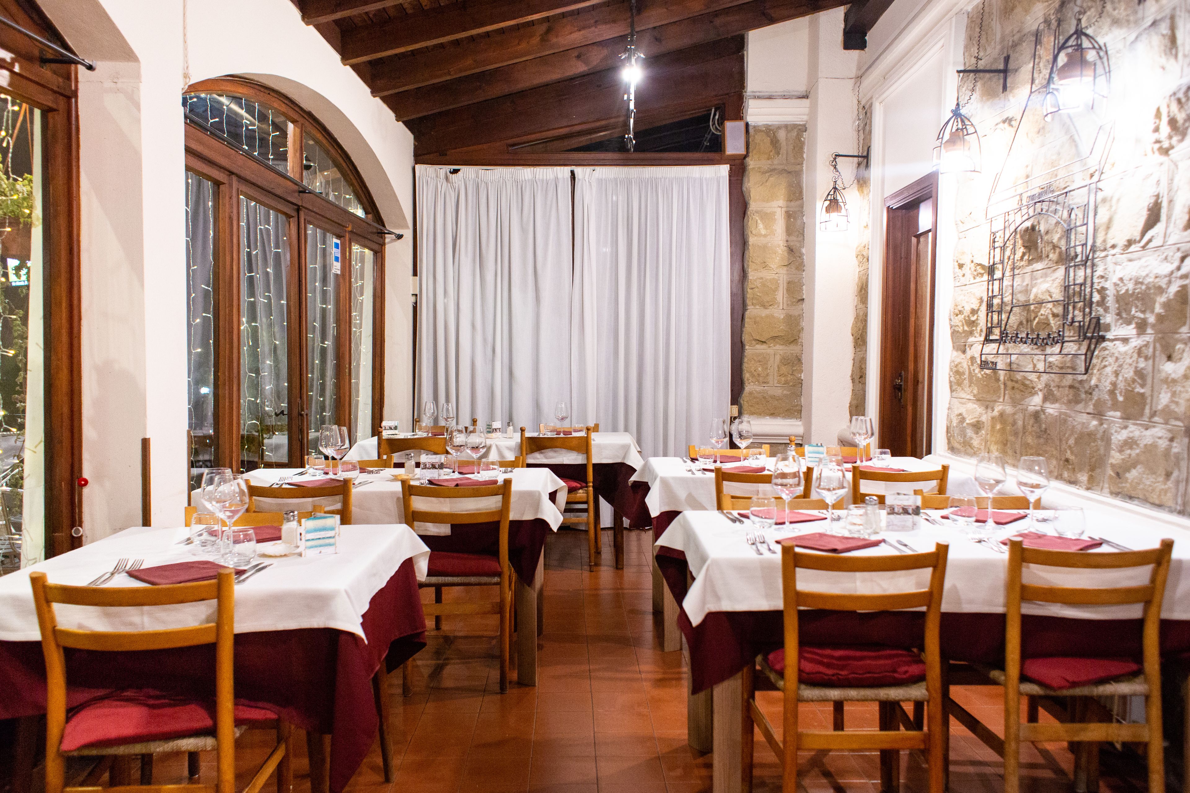 A restaurant with multiple tables set for dining, wooden chairs, and a stone wall.