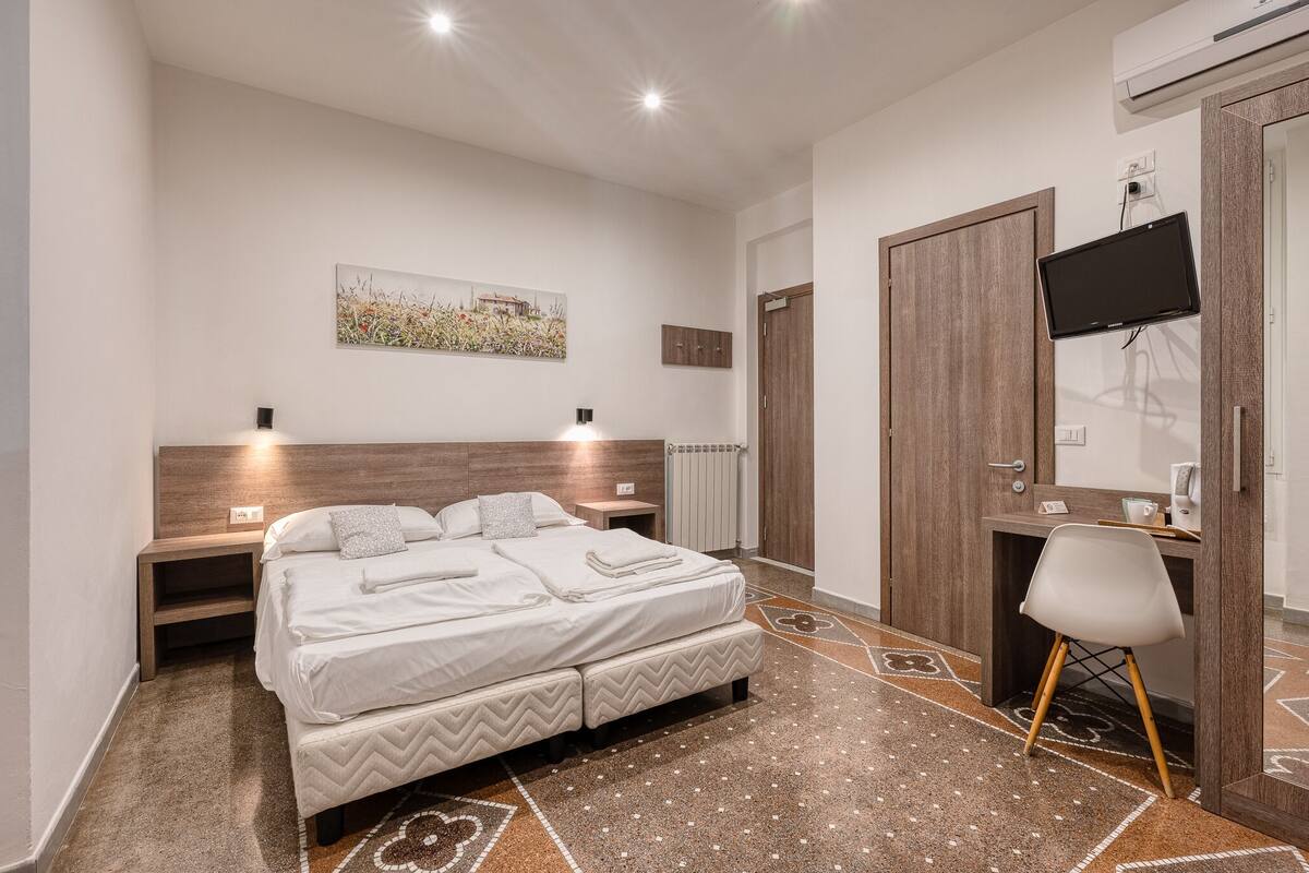 A modern bedroom with a large bed, bedside tables, a desk, and a TV.