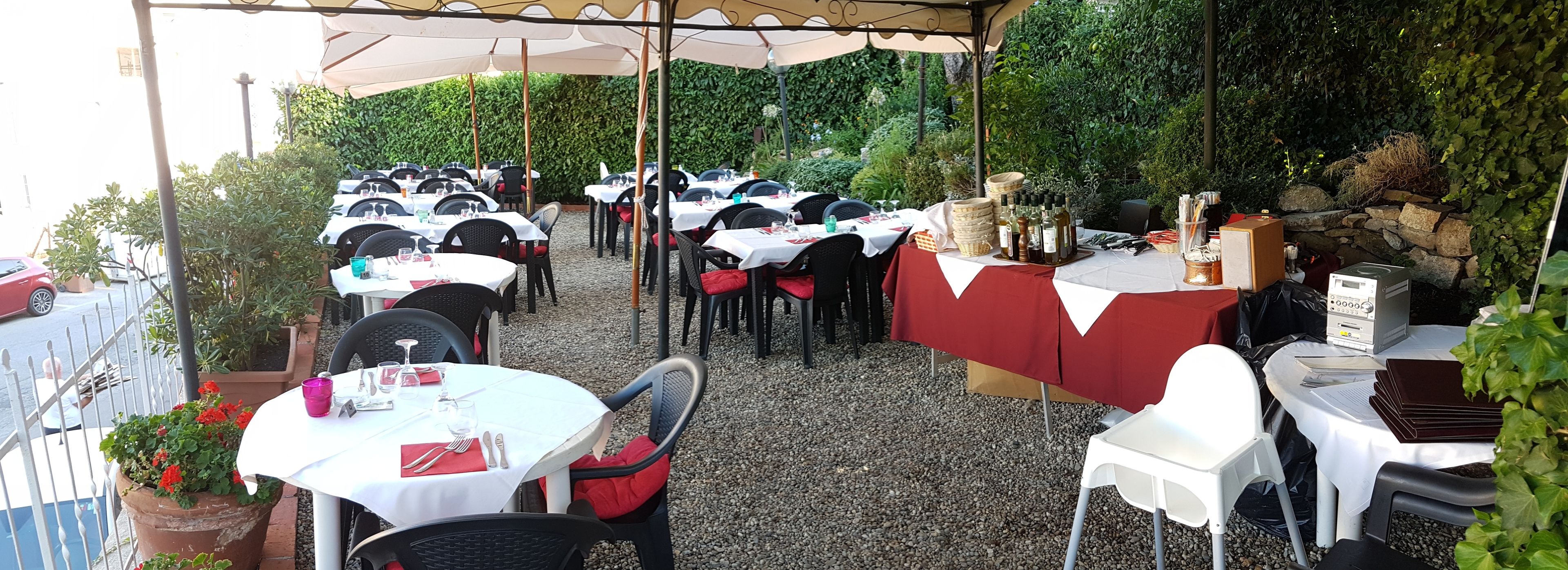 Area esterna con posti a tavola, tavoli e sedie, un bar e un muro di pietra sullo sfondo.
