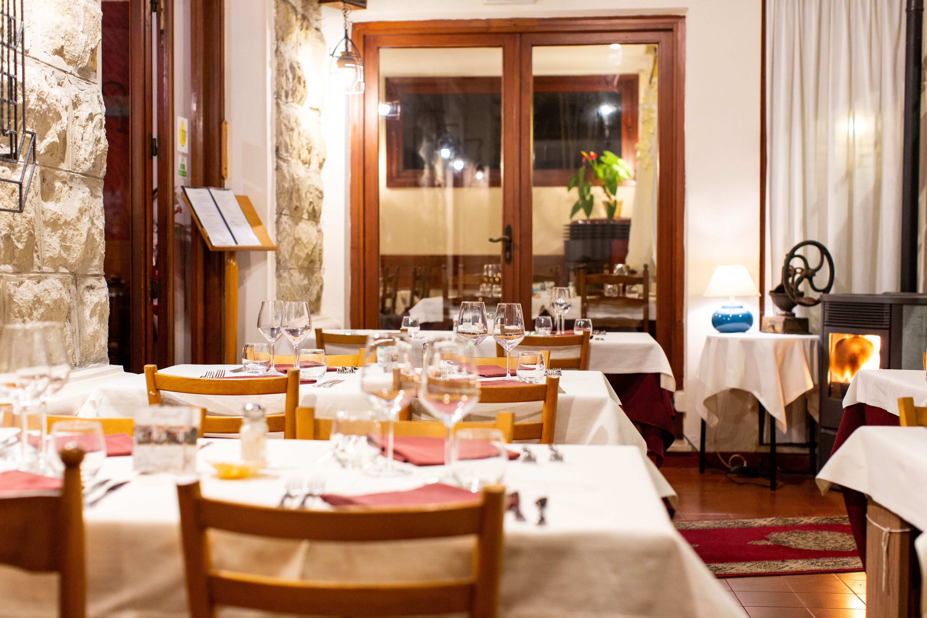 A restaurant with multiple tables set for dining, a stone wall, and a wooden door.