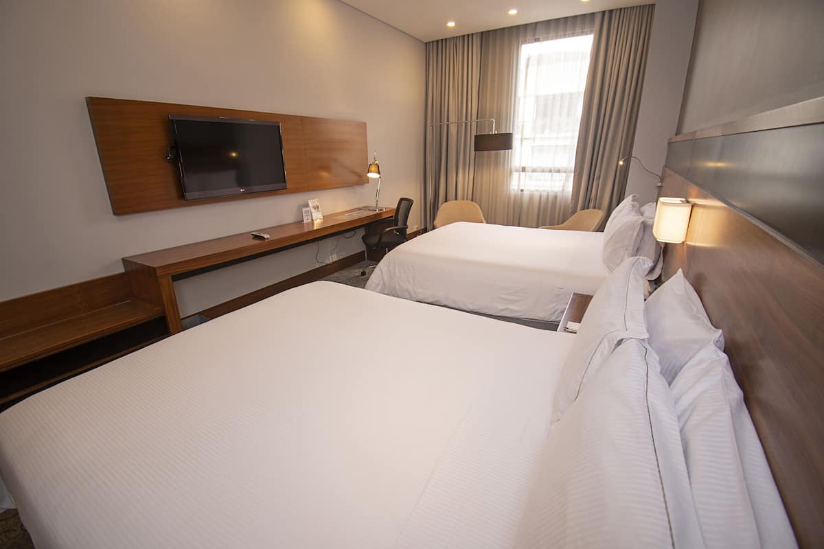 Een hotelkamer met twee bedden, een bureau, een flatscreen-tv en een raam met gordijnen.