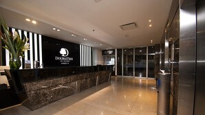 Een moderne hotelreceptie met een marmeren balie, een zwart-wit gestreepte wand en een glazen ingang.