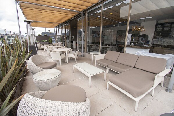 An outdoor seating area with wicker furniture, a glass wall, and a view of the city.