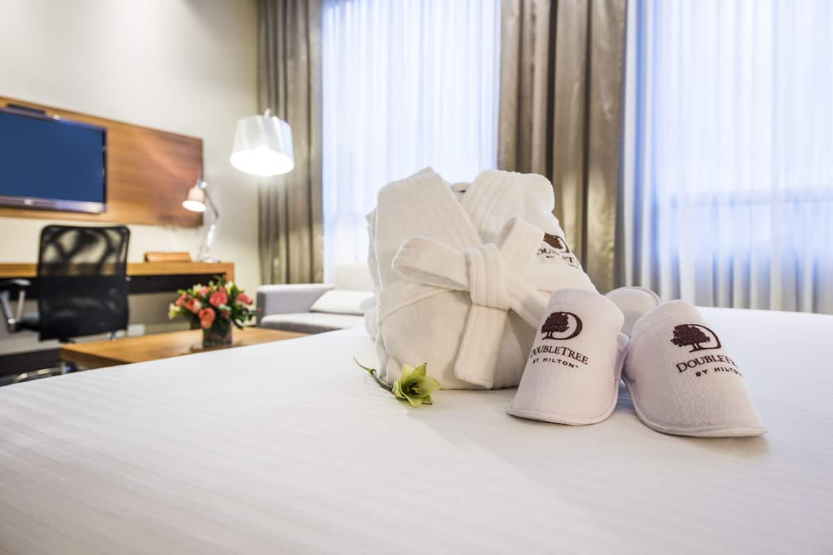 Een hotelkamer met een net opgemaakt bed, een bureau met stoel, een televisie en een raam met gordijnen.