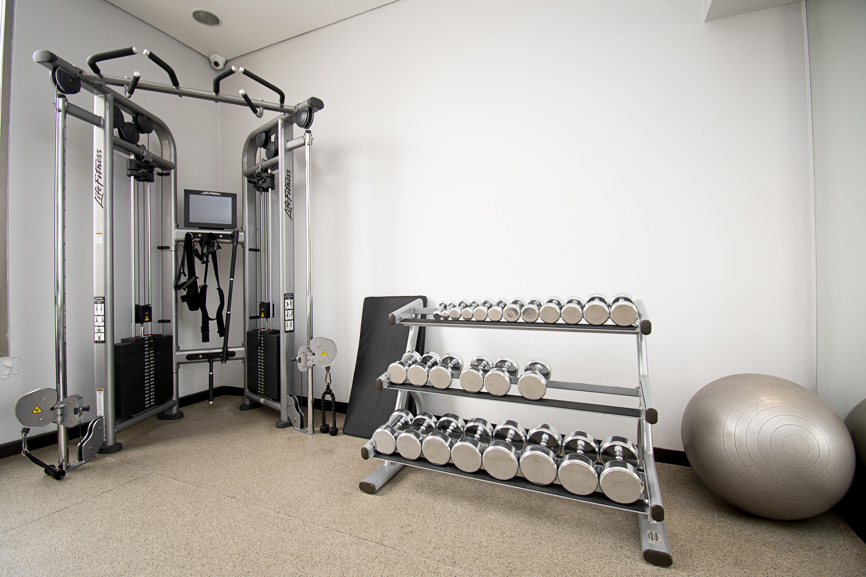 Een fitnessruimte met krachtapparaten, een halterrek en fitnessballen.