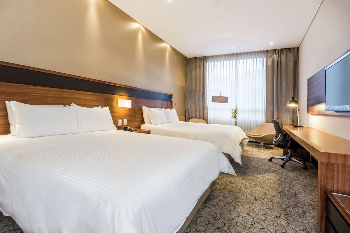 Een hotelkamer met twee bedden, een bureau, een stoel, een televisie en een raam met gordijnen.