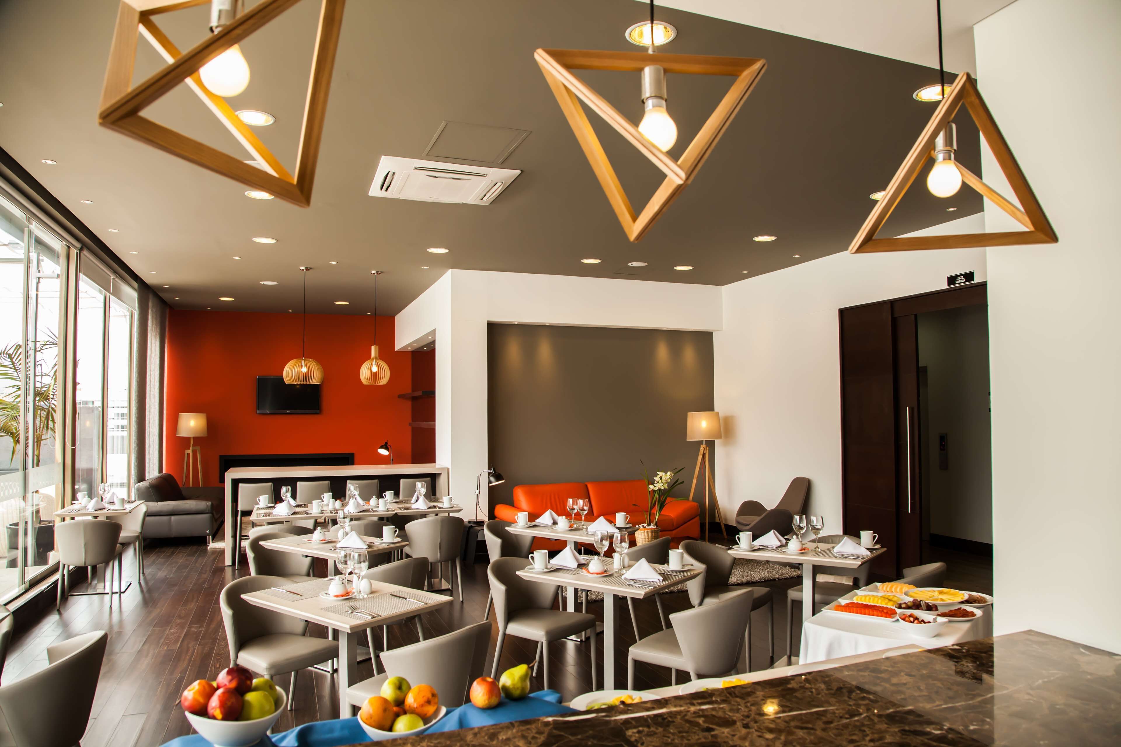 Un comedor moderno con mesas y sillas, un frutero e iluminación colgante.