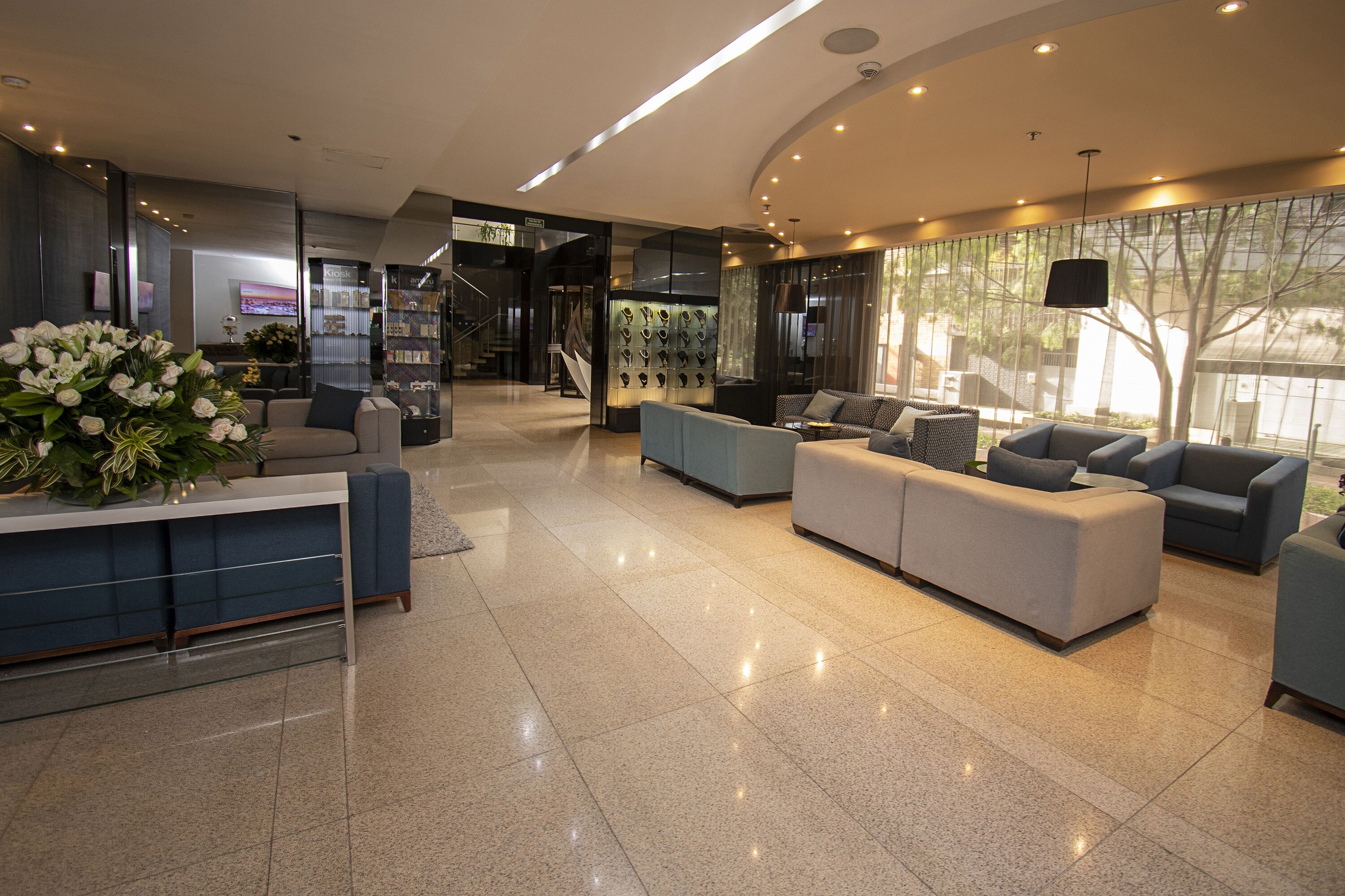 A modern lobby with a reception desk, seating area, and a staircase leading to upper floors.