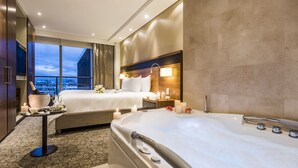 Een hotelkamer met een groot bed, een los bed, een badkuip en uitzicht op de stad.